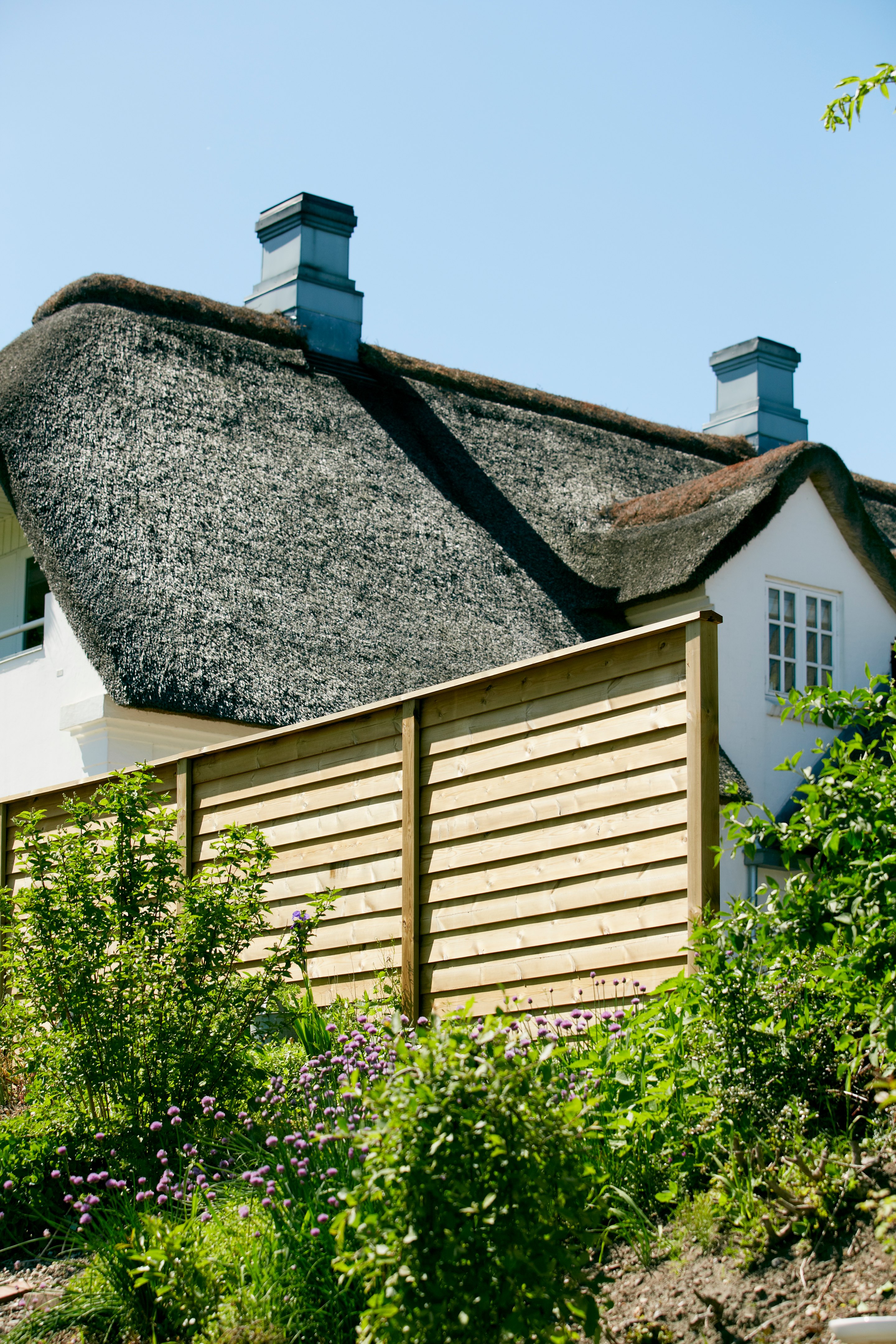 Nordic Fence vor einem reetgedeckten Haus mit Garten